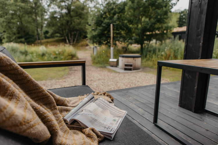 Vista desde una terraza con manta y revista hacia la bañera de hidromasaje en The Hills, Wilsumer Berge, Alemania.