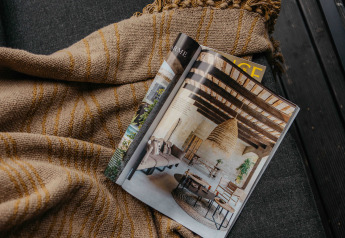 Revista abierta sobre una manta en un alojamiento glamping, mostrando una decoración rústica y acogedora.