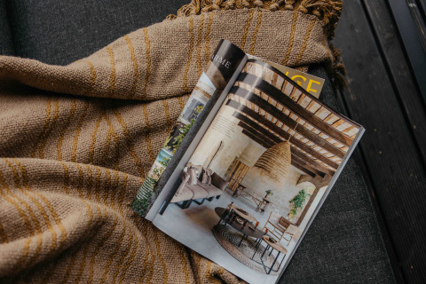 Revista abierta sobre una manta en un alojamiento glamping, mostrando una decoración rústica y acogedora.