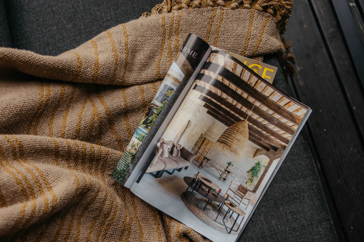 Revista abierta sobre una manta en un alojamiento glamping, mostrando una decoración rústica y acogedora.