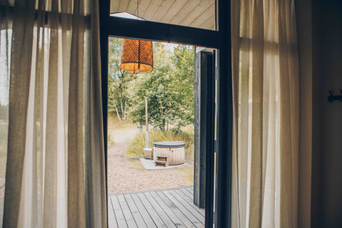 Vista desde una tiny house hacia el jacuzzi exterior en Wilsumer Berge, Alemania, puerta abierta.
