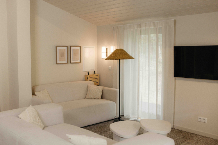 Sala de glamping luminosa con sofás blancos, lámpara de pie, cuadros, televisor y cortinas traslúcidas.