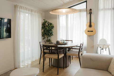 Gezellige eetruimte in tiny house met ronde tafel, gitaar aan de muur en veel licht, Wilsumer Berge, Duitsland.