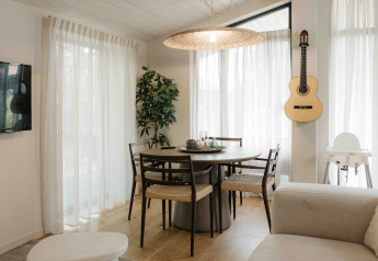 Comedor luminoso en mini casa con mesa redonda, guitarra en la pared y grandes ventanales, Wilsumer Berge, Alemania.