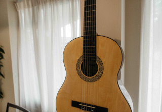 Akoestische gitaar in een zonnige ruimte met gordijnen in The Hills tiny house aan Wilsumer Berge, Duitsland.