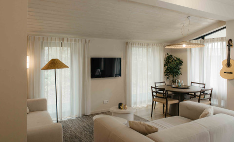 Acogedora sala de glamping con sofás claros, mesa de comedor, guitarra en la pared y luz natural.