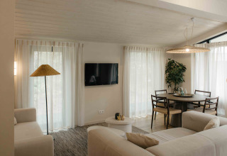 Acogedora sala de glamping con sofás claros, mesa de comedor, guitarra en la pared y luz natural.