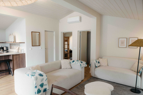 Lichte glamping leefruimte met comfortabele zetels, open keukenhoek en zicht op een kamer met stapelbed.