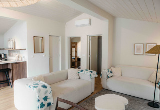 Lichte glamping leefruimte met comfortabele zetels, open keukenhoek en zicht op een kamer met stapelbed.
