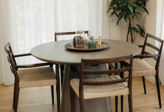 Ronde eettafel met vier stoelen, stijlvol dienblad, lichte houten vloer en hoge witte gordijnen.