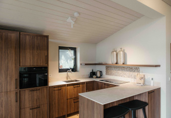 Cocina moderna de glamping con armarios de madera, encimeras blancas y dos taburetes negros.