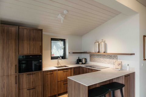 Cocina moderna de glamping con armarios de madera, encimeras blancas y dos taburetes negros.