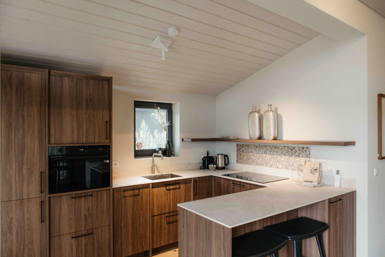 Cocina moderna de glamping con armarios de madera, encimeras blancas y dos taburetes negros.