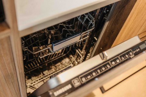 Lavavajillas abierto en un alojamiento glamping, integrado en un moderno armario de madera y metal.