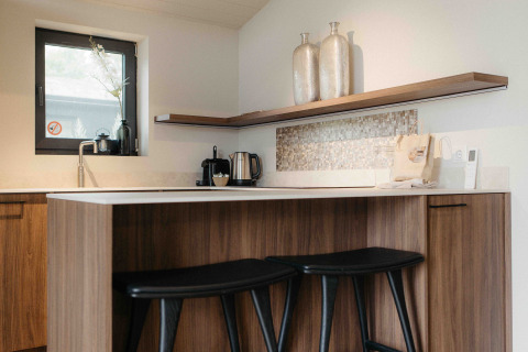 Moderne glampingkeuken met houten kasten, barkrukken, decoratieve vazen en klein raam.