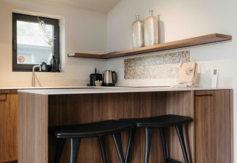 Moderne glampingkeuken met houten kasten, barkrukken, decoratieve vazen en klein raam.