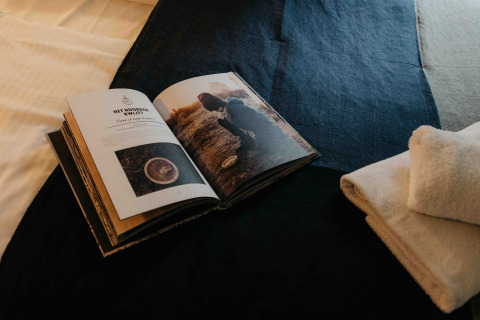 Open boek en gevouwen handdoeken liggen op een bed in een glampingverblijf met een warme, gezellige sfeer.