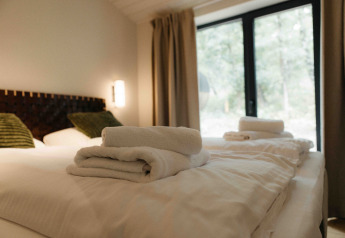 Alojamiento glamping con cama cómoda, toallas limpias, cojines verdes y ventanales con vista a la naturaleza.
