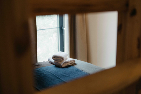 Stapeltje handdoeken op een bed, door een raam gezien in een tiny house te Wilsumer Berge, Duitsland.