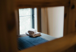 Stapeltje handdoeken op een bed, door een raam gezien in een tiny house te Wilsumer Berge, Duitsland.