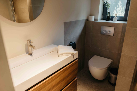 Stijlvolle badkamer in een glamping verblijf met zwevend toilet, wastafel, spiegel en raam.