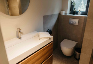 Stijlvolle badkamer in een glamping verblijf met zwevend toilet, wastafel, spiegel en raam.