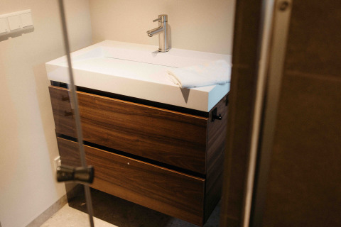 Moderne badkamerkast met houten laden en witte lavabo in een glampingverblijf, deur halfopen.