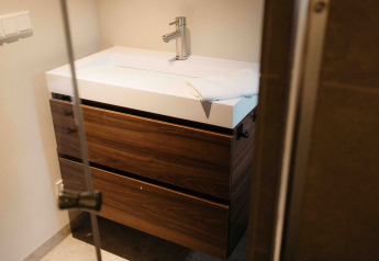 Moderne badkamerkast met houten laden en witte lavabo in een glampingverblijf, deur halfopen.