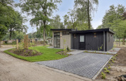 Modern lodge with dark exterior and large glass windows, surrounded by trees and a well-kept lawn.