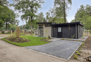 Moderne lodge met donkere gevel en grote ramen, omringd door bomen en een goed onderhouden grasveld.