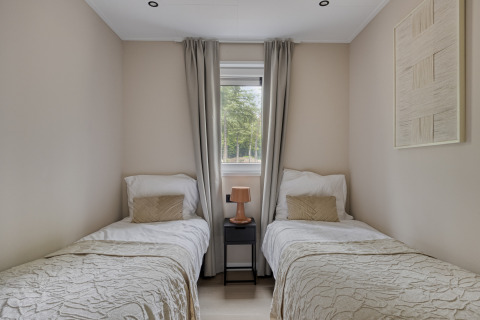 Schlafzimmer mit zwei Einzelbetten, Nachttisch und Fenster in Heidehof 5 personen, Bospark Ede, Niederlande.