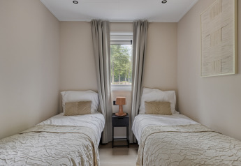 Schlafzimmer mit zwei Einzelbetten, Nachttisch und Fenster in Heidehof 5 personen, Bospark Ede, Niederlande.