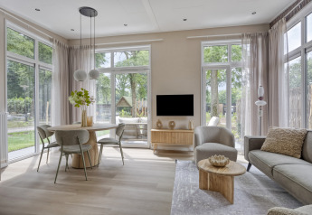 Moderne stue med store vinduer, spisebord og sofa i en lodge på Bospark Ede, Heidehof 5 personen, Nederlandene.