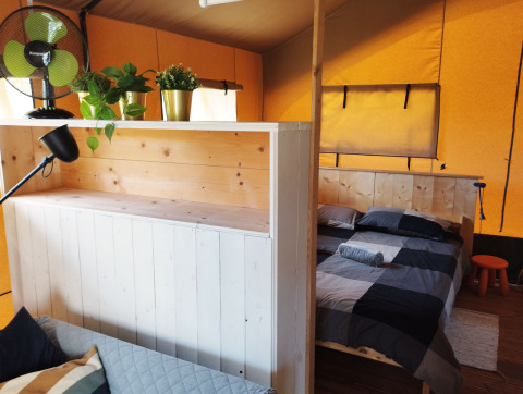 Interior of a safari tent with divided living and sleeping areas at Camping Suasa in Italy, featuring plants and a fan.