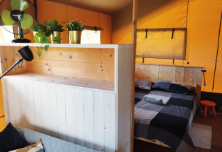Interieur van een safaritent met aparte woon- en slaapruimte op Camping Suasa in Italië, met planten en ventilator.