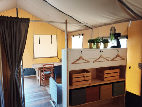 Inside view of a safari tent with wooden furniture, plants, and a fan at Camping Suasa in Italy.