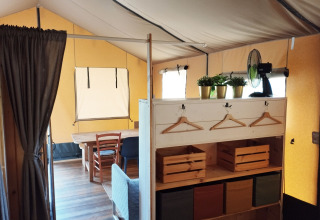 Binnenkant van een safaritent met houten meubels, planten en ventilator bij Camping Suasa in Italië.