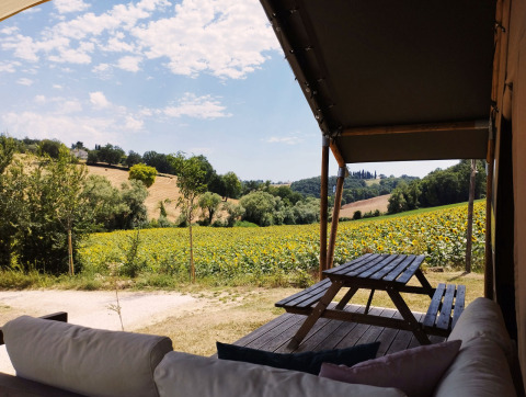 Uitzicht vanuit een safaritent met bank en picknicktafel op zonnige velden bij Camping Suasa, Italië.