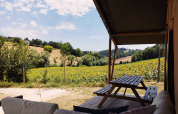 View from a safari tent with sofa and picnic table overlooking sunny fields at Camping Suasa, Italy.