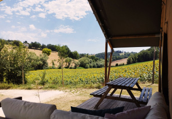 Uitzicht vanuit een safaritent met bank en picknicktafel op zonnige velden bij Camping Suasa, Italië.