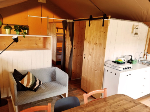 Interieur van een safaritent met bank, eettafel, keuken en stapelbed bij Camping Suasa in Italië.