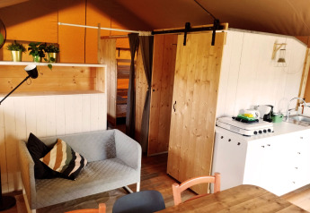 Interior of a safari tent with sofa, dining table, kitchen, and bunk bed at Camping Suasa in Italy.