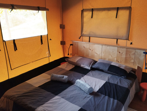 Interieur van een safaritent met tweepersoonsbed, houten hoofdbord en ramen op Camping Suasa in Italië.