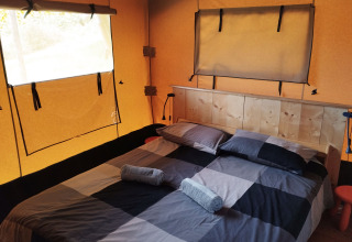 Interior of a safari tent with a double bed, wooden headboard, and windows at Camping Suasa in Italy.