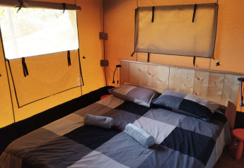 Interieur van een safaritent met tweepersoonsbed, houten hoofdbord en ramen op Camping Suasa in Italië.