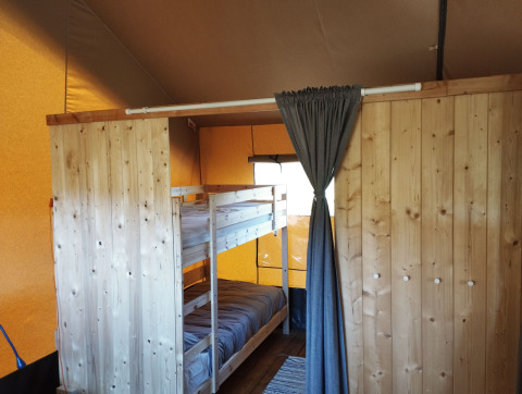 Interior view of a safari tent bedroom with bunk bed and wooden partition at Camping Suasa, Italy.