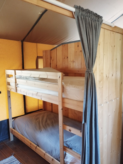 Interior view of a safari tent at Camping Suasa in Italy, featuring wooden bunk beds and a curtain.