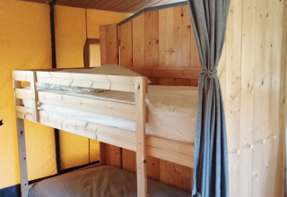Interior view of a safari tent at Camping Suasa in Italy, featuring wooden bunk beds and a curtain.