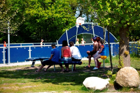 Tieners zitten op een bankje bij een blauwe basketbalveld in vakantiedorp ’t Strandheem in Groningen, Nederland.