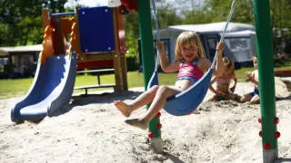 Bambini che giocano nell’area giochi con altalene e scivolo al parco vacanze ’t Strandheem a Groningen.